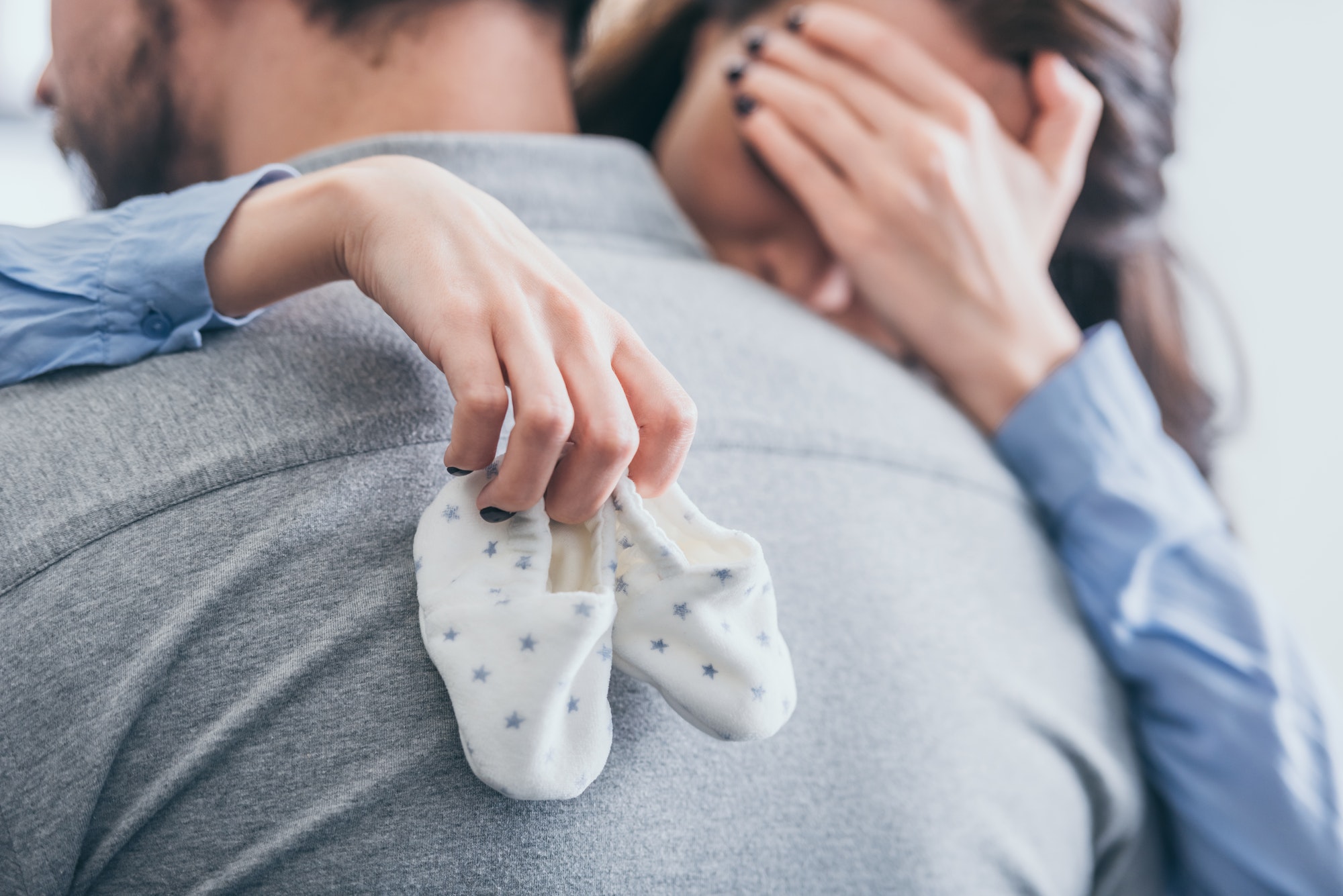 cropped view of woman, hugging man, holding baby socks and crying in room, grieving disorder concept